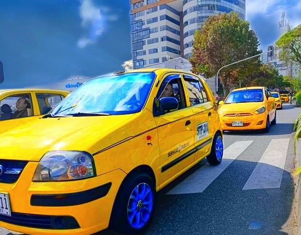 Taxis tradicionales circulando en una avenida urbana de Pitalito con edificios al fondo.
